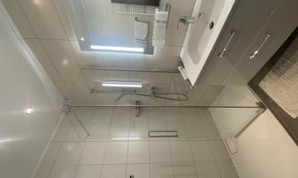 A modern bathroom with a glass shower and bright tiled floor. The room is well-lit and has an elegant sink line.