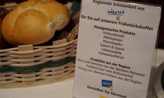 A basket with fresh rolls and regional delicacies. Next to the basket is a sign with information about the breakfast buffet and the products offered.