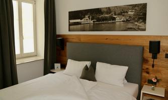 A modern bedroom with a cozy bed and a gray headboard. On the wall hangs a black-and-white picture of a landscape by the water.