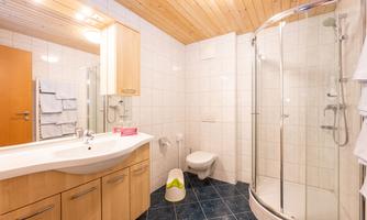 A modern bathroom with a shower and a wooden sink. The walls are tiled in light colors and the ceiling is made of wood.