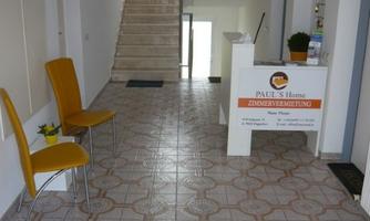 A bright entrance with tiled floor and a reception desk. To the left are two yellow chairs and a plant.
