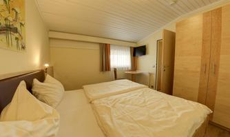 A cozy bedroom with two single beds and neutral decor. The room features windows with natural light and a small seating area.