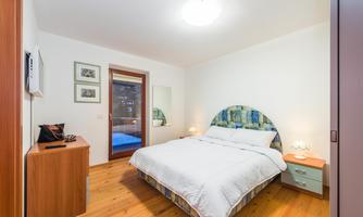 A cozy bedroom with a large bed and wooden floor. Next to the bed is a nightstand and a wooden wardrobe.