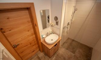 A modern bathroom with a shower and a sink. The walls are brightly tiled and the door is made of wood.