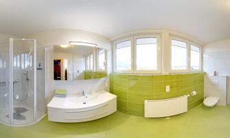 A modern bathroom with green tiles and plenty of daylight. It features a shower, a sink, and large windows.
