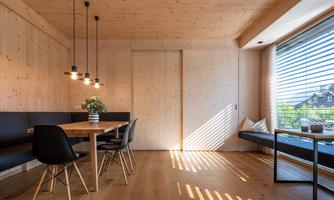 A modern dining kitchen with wooden walls and a large window. The table is simple and inviting, surrounded by elegant chairs.