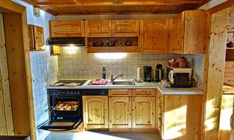 A cozy kitchen with wooden furniture and modern appliances. The stove is in use and there is a window that lets in daylight.