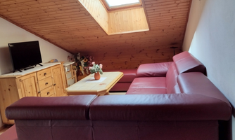 A cozy living room with a red sofa and a wooden table. A skylight ensures plenty of daylight.
