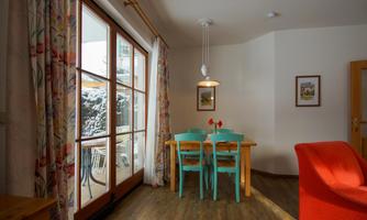 A cozy dining area with a wooden table and colorful chairs. Large windows let in plenty of daylight and provide a view of the snow outside.