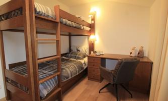 A room with a loft bed and a desk. The walls are light, and there is cozy lighting.