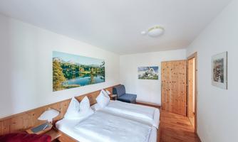 A cozy hotel room with two single beds and warm wood paneling. Landscape pictures hang on the walls, creating a relaxing atmosphere.