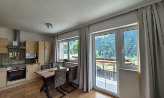 A bright and modern kitchen with a dining table and chairs. Through the windows, there is a beautiful view of the mountains.