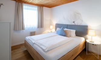 A modern bedroom with a comfortable bed and soft lighting. Bright walls and large windows create a cozy atmosphere.