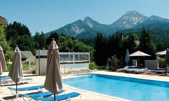 A beautiful pool area with deck chairs and sun umbrellas. Majestic mountains can be seen in the background.