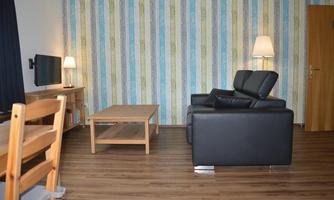 A modern living room with a black sofa, a wooden table, and a television. The wall is decorated with colorful stripes, and the lighting creates a cozy atmosphere.