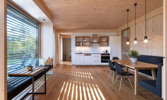 A modern kitchen with wood paneling and a dining area. Bright space with large windows and natural light.