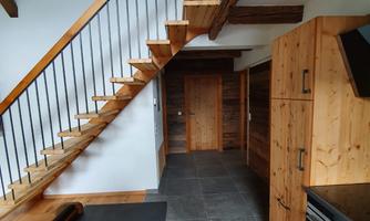 A modern kitchen with wooden furniture and a sleek, gray floor. A staircase leads to the upper area of the house.