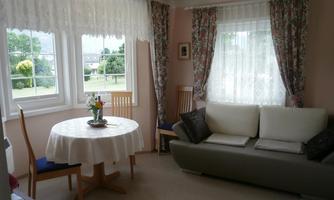 A cozy room with a round table and two chairs. On the table sits a flower vase, while a couch invites you to relax.
