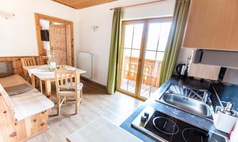 A cozy kitchen with wooden paneling and a dining area. Large windows offer a view of the balcony and let in plenty of light.