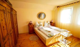 A bright bedroom with two beds and a wooden wardrobe. The walls are painted yellow and there is a painting on the wall.