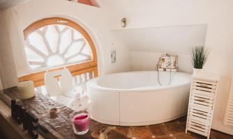 A bright bathroom with a round bathtub and natural wood details. A large window ensures plenty of light and a relaxing atmosphere.