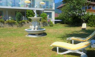 A beautiful garden with a fountain and loungers. In the background, balconies with sun umbrellas can be seen.