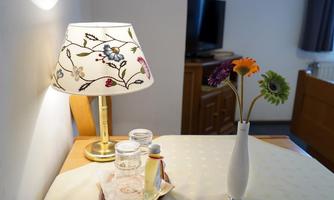 A table with a decorative lamp and a vase of colorful flowers. Next to it are glasses and a small bowl on a tablecloth.