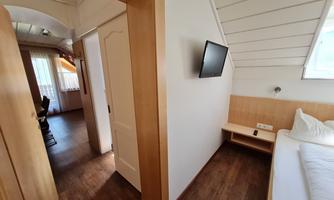 A bright room with wooden paneling and a television on the wall. The room has access to another area and offers a cozy atmosphere.