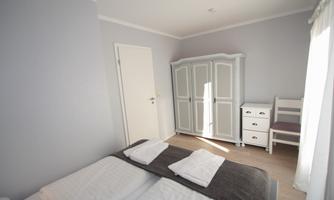 A bright bedroom with two beds and fresh towels. The room has a wardrobe, a table, and a chair.