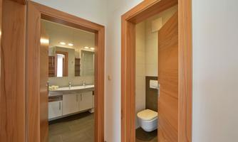 A bright bathroom with modern fixtures and a large mirror. On the right, a separate toilet is visible.