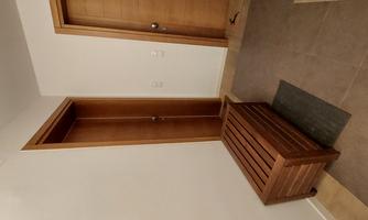 A bright hallway with two wood-colored doors and a wooden bench. The floor is tiled and covered with a small rug.