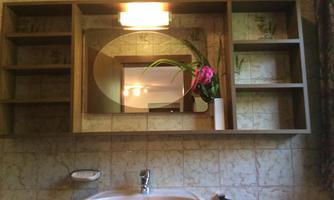 A bathroom with a round mirror and wooden shelves. On the sink is a small bouquet of flowers.