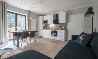 A modern kitchenette with a cozy dining area and a sofa. The room has large windows that let in plenty of daylight.