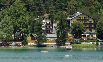A tranquil lake with some boats and surrounding trees. In the background, several buildings can be seen in a picturesque setting.