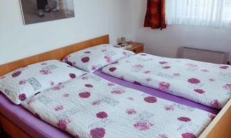 A cozy bedroom with a double bed and colorful blankets. A piece of art hangs on the wall, and the window lets in plenty of light.