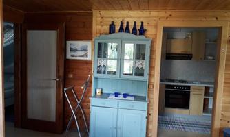 A cozy room with wooden paneling and a blue display cabinet. In the background, there is a modern kitchen and a door to another room.