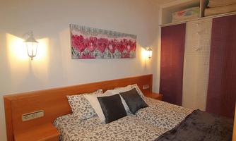 A cozy bedroom with a large bed and decorative pillows. A picture with colorful flowers hangs on the wall.