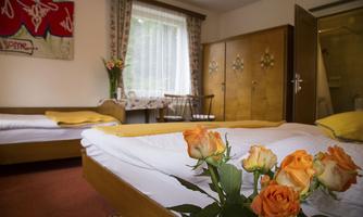 A cozy room with two beds and a small table. Fresh roses in various colors are lying on the bedspread.