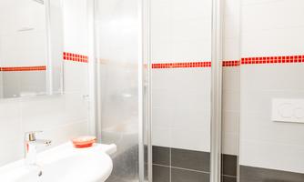 A modern bathroom with a shower cabin, a sink, and a toilet. The walls are brightly tiled, with an accent in red.