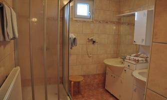 A modern bathroom with a shower, sink, and a small stool. The walls are adorned with bright tiles, and there are towels nearby.
