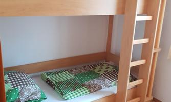 A room with a loft bed made of light wood. On the bed are pillows with colorful covers.