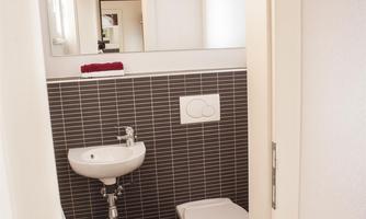 A modern bathroom with dark tiles. There is a sink and a toilet, as well as a large mirror.