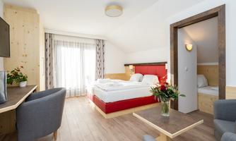 A modern room with a double bed and a separate living area. Large windows provide plenty of daylight and a cozy atmosphere.