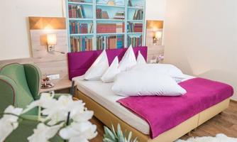 A cozy bedroom with a large bed and colorful cushions. A selection of fresh fruits is on the table.