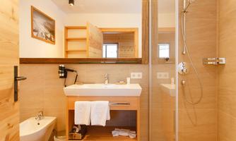 A modern bathroom with wood accents and clean lines. It features a sink, a shower, and a toilet.