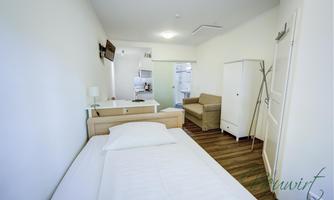 A simple and modern room with a single bed, a desk, and a sofa. The bright decor creates an inviting atmosphere.