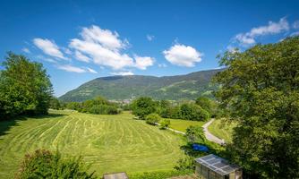 A picturesque landscape with gentle hills and green meadows. The sky is clear and blue, while some clouds drift by.