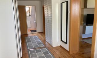 A bright hallway with wooden floors and several doors. Gray runners lie on the floor, and there is a large mirror on the wall.