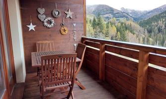 A cozy wooden balcony with a table and chairs. In the background, there are mountains and trees.