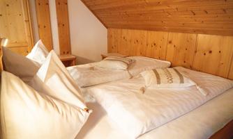 A cozy bedroom with wood paneling and a double bed. The pillows are decorative and the atmosphere is inviting.